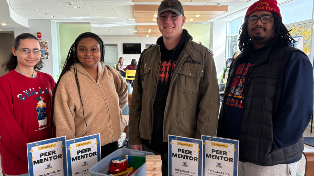 Four peer mentors are photographed in the PHS building with their signs on the table.